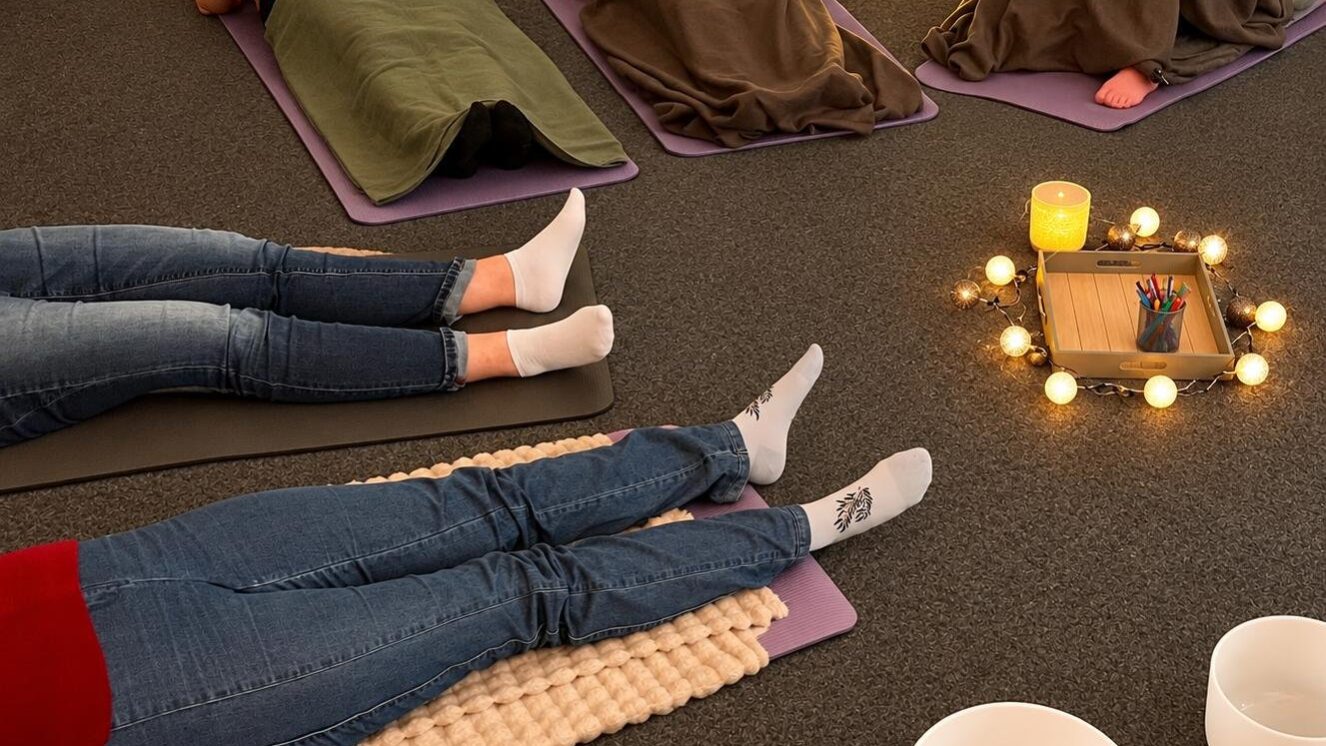 Teilnehmende beim Entspannungskurs Teilnehmende liegen entspannt auf Matten und Decken während eines Entspannungskurses mit Kerzenlicht und Klangschalen